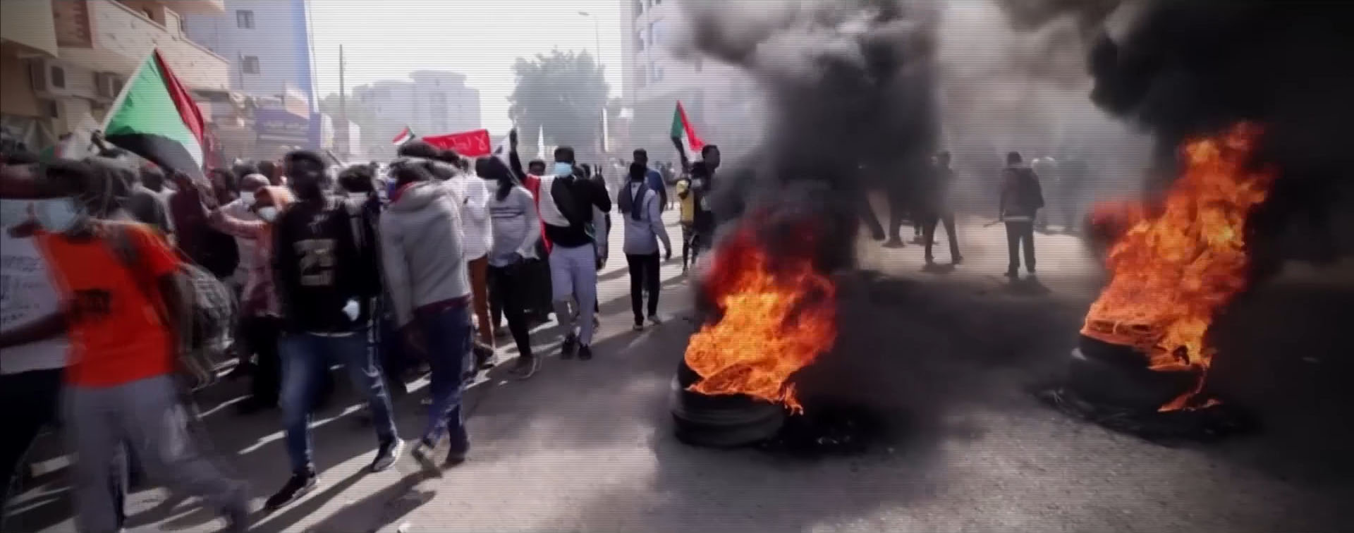 Protesters in Sudan carrying their country's flags and burning tires