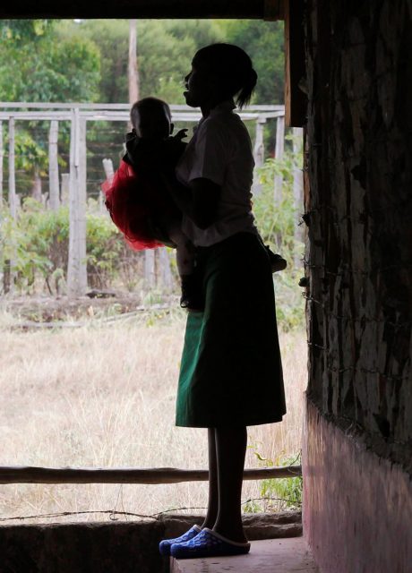 A teenage girl stands outside her class with her baby inn Tanzania