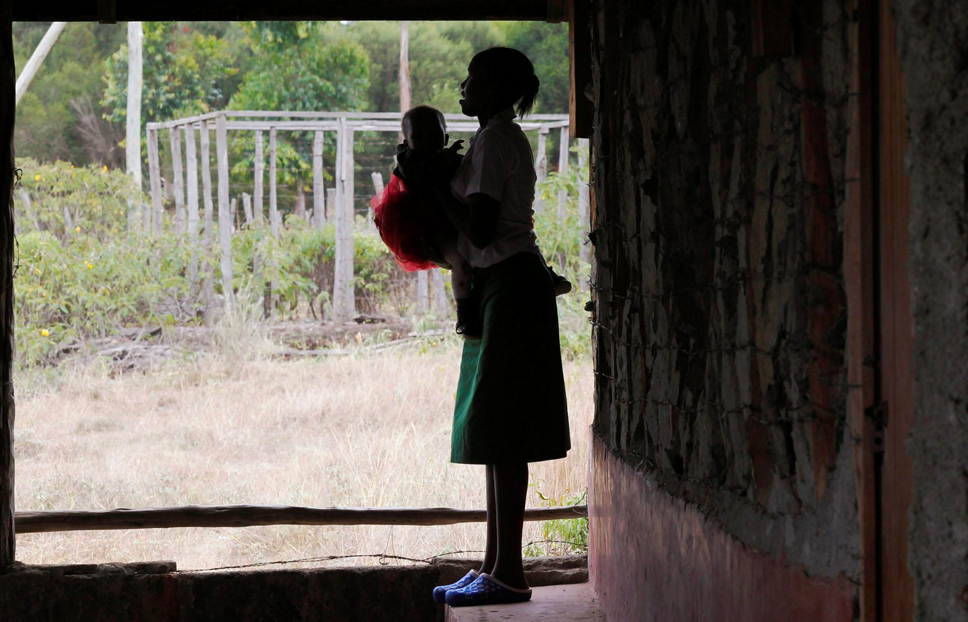 A teenage girl stands outside her class with her baby in Tanzania