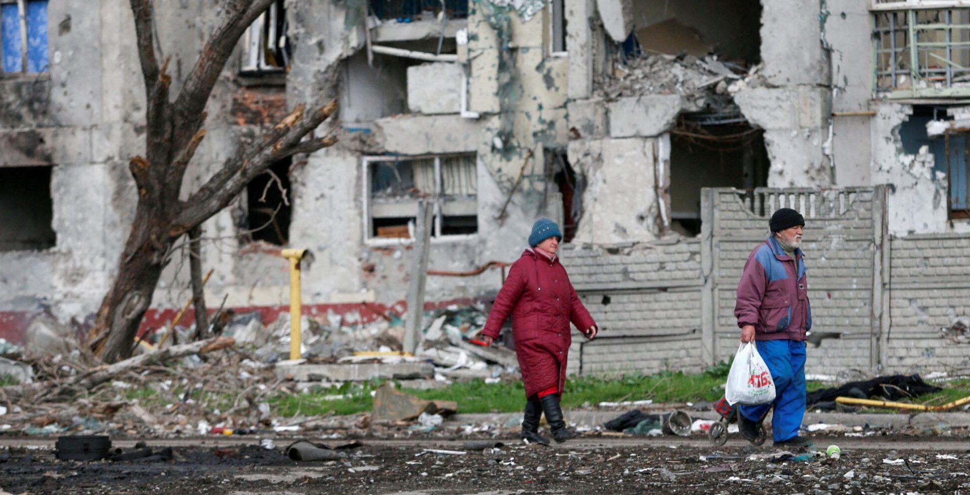 A man and a woman walk by destroyed residential buildings in Ukraine