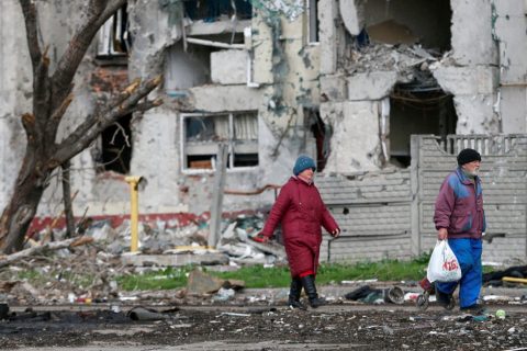 A man and a woman walk by destroyed residential buildings in Ukraine