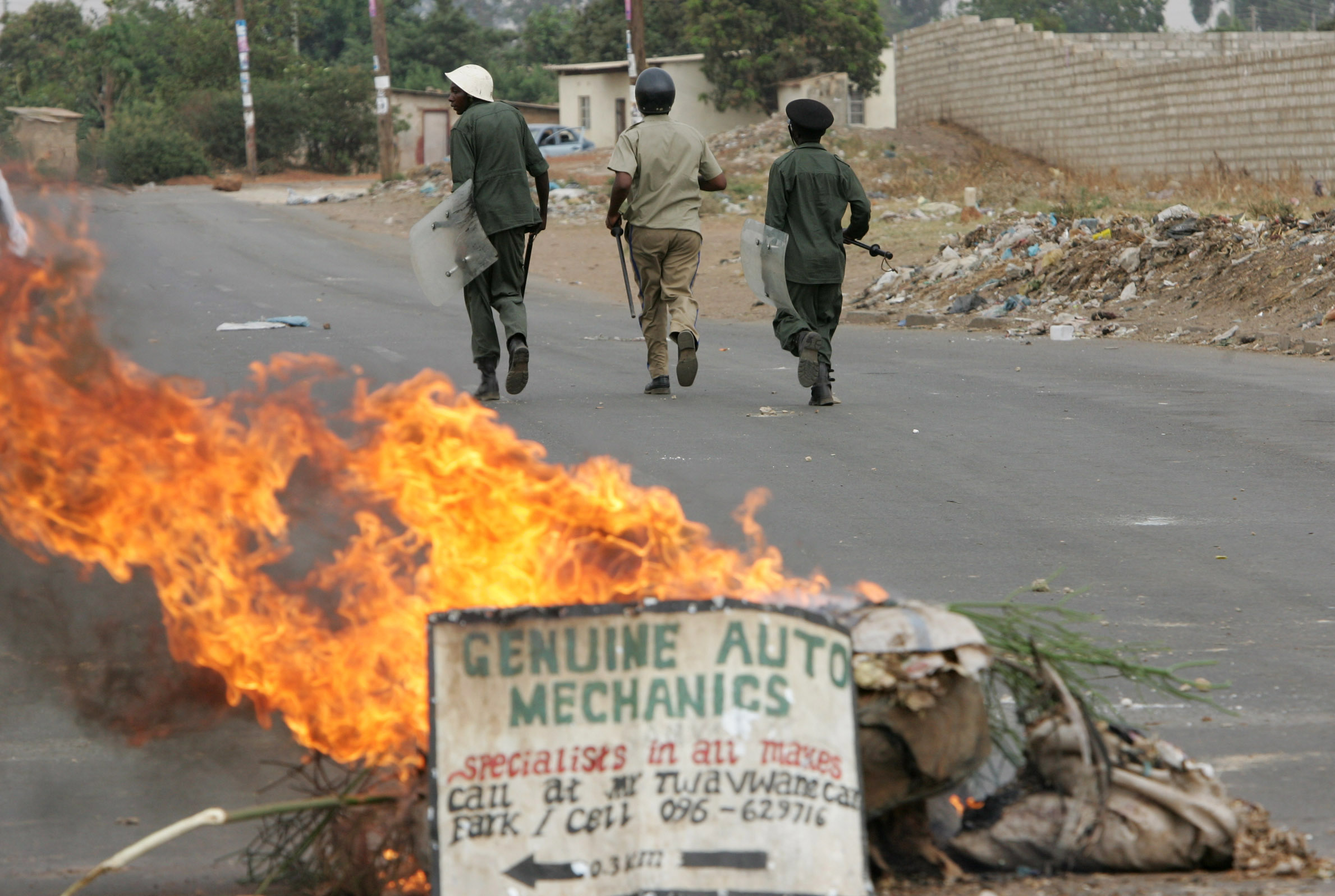 Three policemen sprinting past a burning barricade during a protests in Zambia
