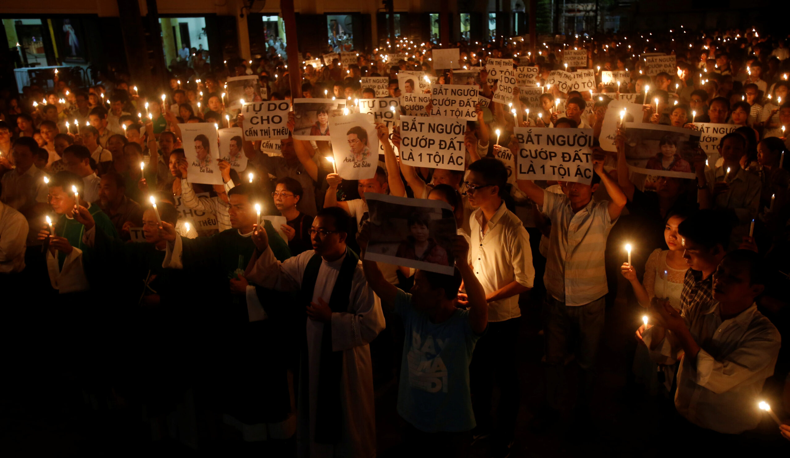 Vietnamese protesters hold images of dissident blogger Nguyen Huu Vinh and land protection activist Can Thi Theu during a mass prayer to call for justice in their trials at Thai Ha church in Hanoi