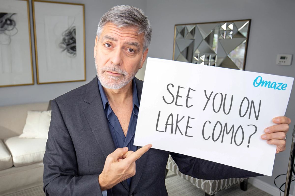 George Clooney holds a sign that reads "see you on Lake Como?"