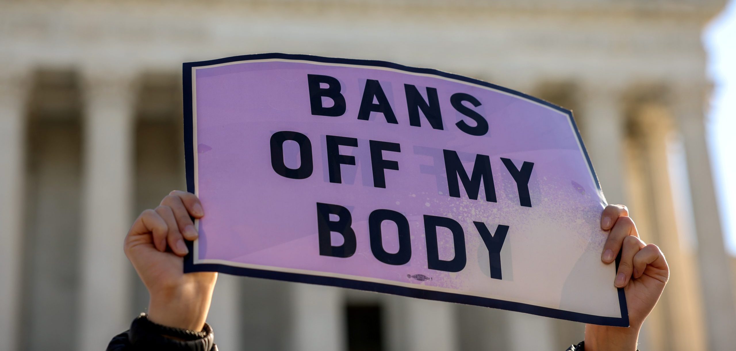 Someone's hands hold a sign that reads 'Bans off my body'