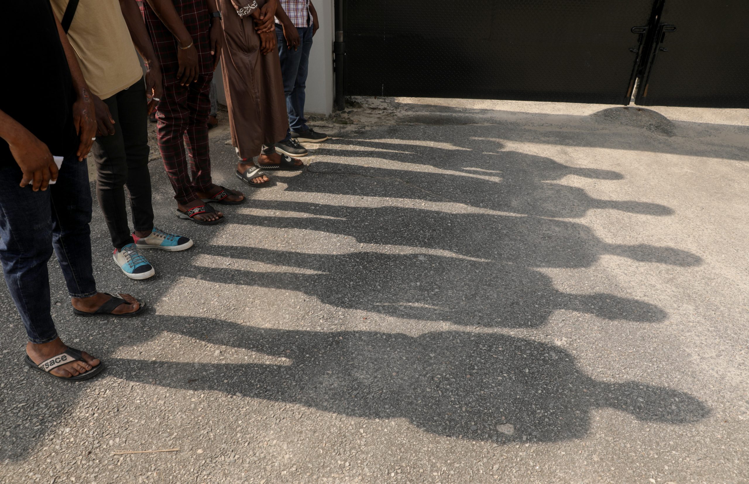 Four men stand side by side and their shadows are seen on the ground
