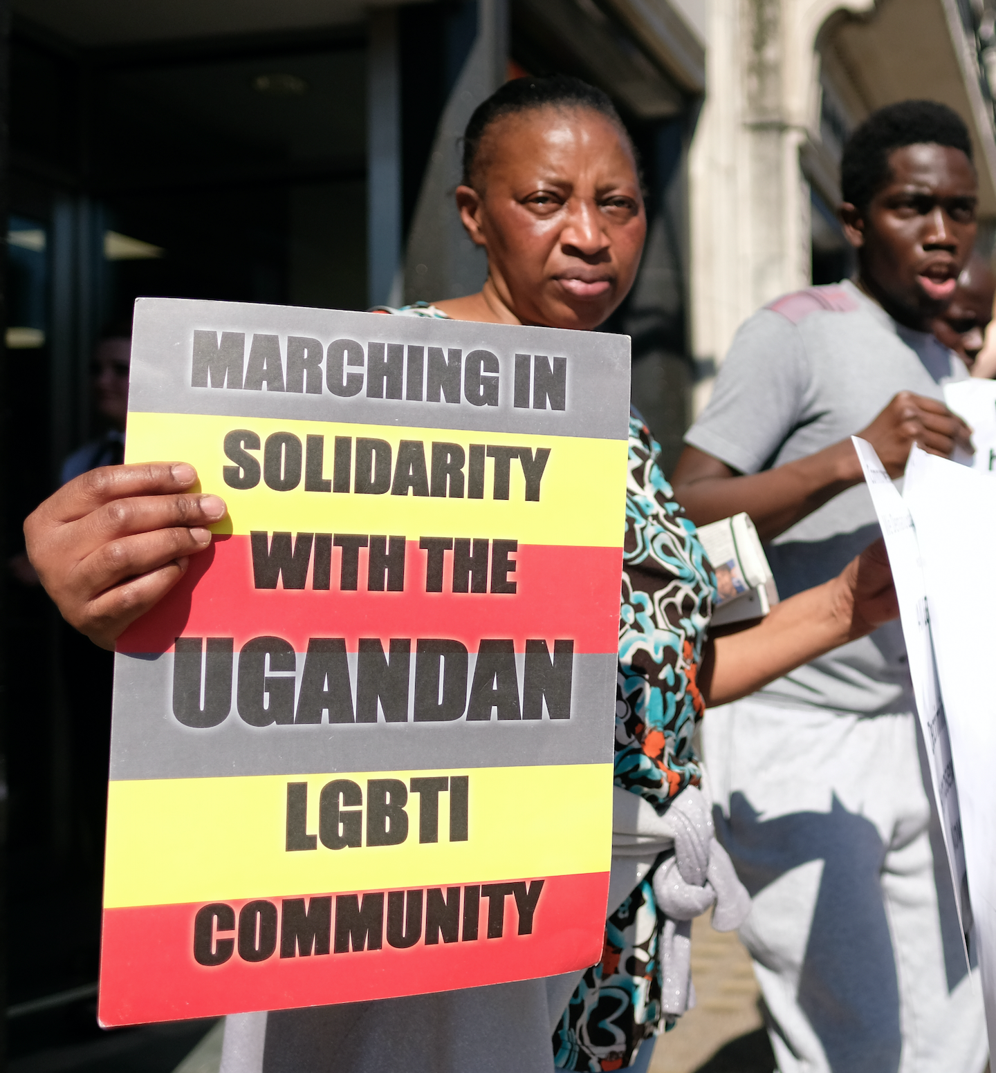A woman and a man participating in a protest for LGBT rights in Uganda. She holds a sign that reads: "Marching in Solidarity with the Ugandan LGBTI community"