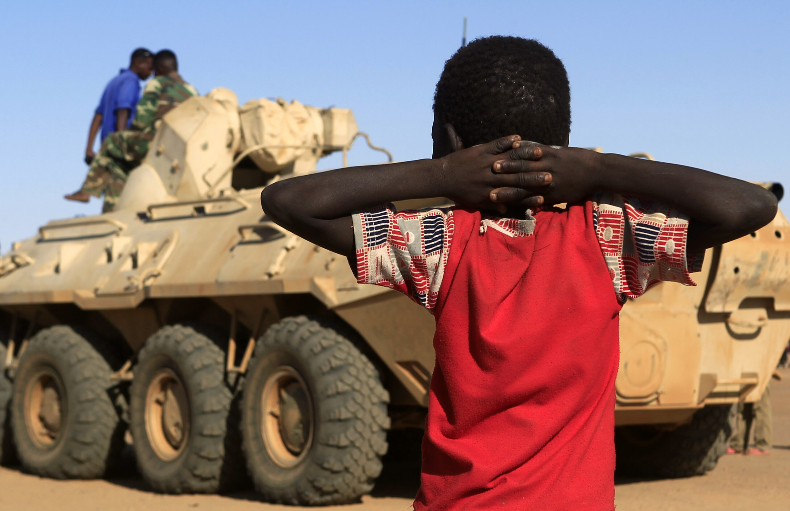 A boy looks at a military convoy of government forces in North Darfur