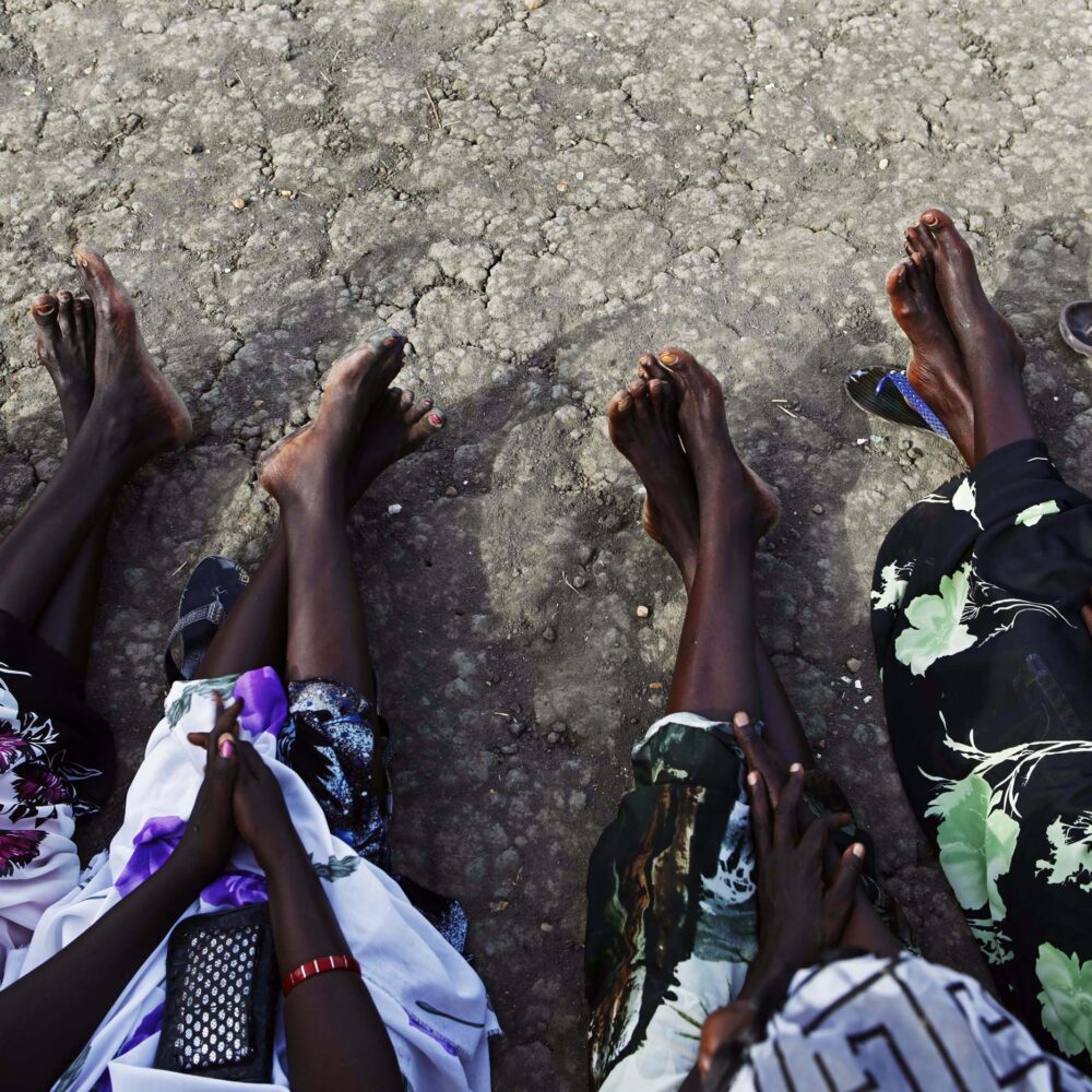 Sudanese women sit barefoot while waiting in line outside a polling station in Malakal