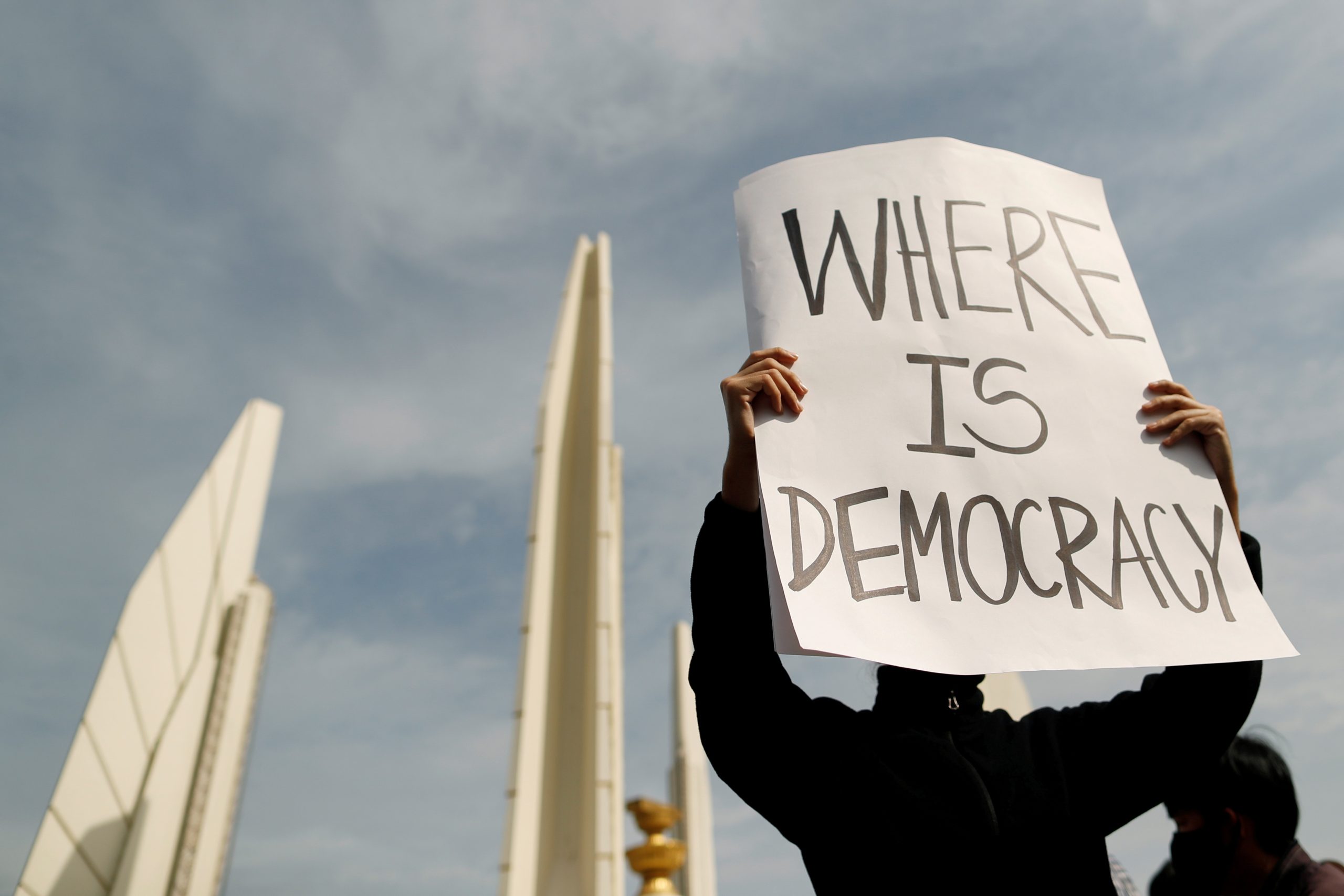A protester's face is hidden behind a sign he is carrying that reads 'Where is democracy'