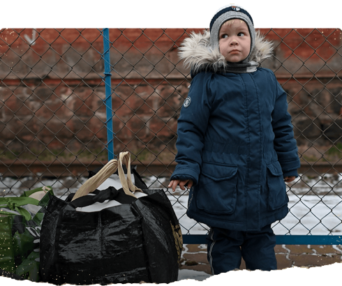 A child stands next to a bag containing his belongings