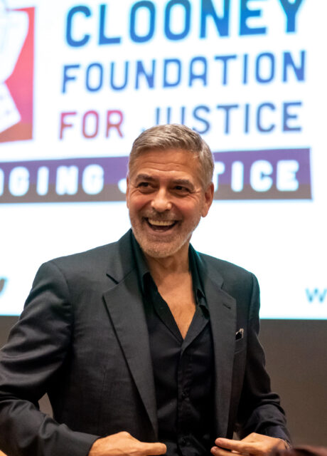 George Clooney stands in front of a large CFJ logo