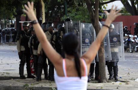 A woman walks past with her arms up in front of police as they clashes with anti-government protesters at Altamira square in Caracas
